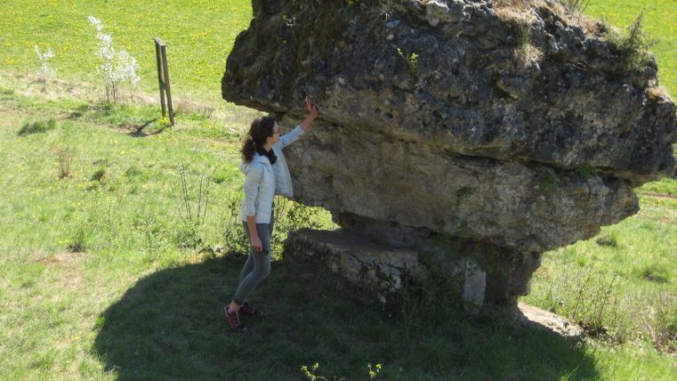 A woman stands at the "Hippelsteinchen" formation in a meadow 