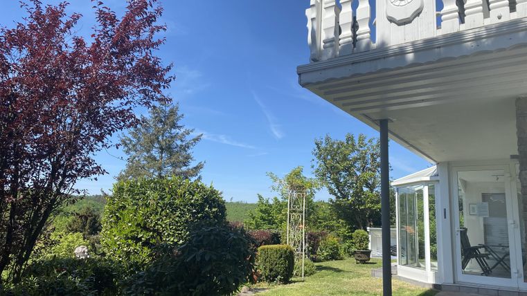A modern house with a beautiful garden. The sky is clear and blue, surrounded by green plants.