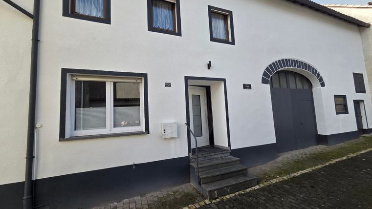 Une maison moderne avec une façade lumineuse et de grandes fenêtres. L'escalier mène à l'entrée, à côté se trouve une grande allée.