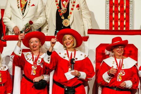 Three women in red costumes and hats are happily celebrating. They are holding glasses in their hands and smiling at the camera.