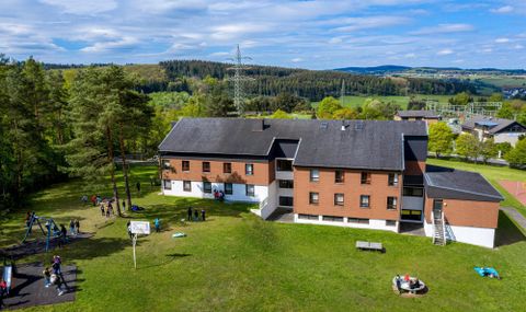A view from above of the Gerolstein Youth Hostel building. Around it is a green meadow, children are playing on it!