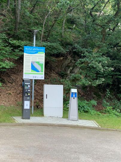 Eine Ladestation für Elektrofahrzeuge in einer grünen Umgebung. Neben der Station befindet sich ein Informationsschild.