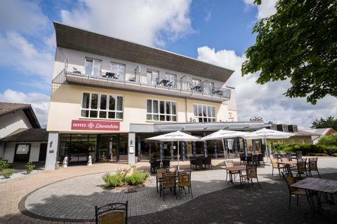 Ein modernes Hotel mit einer einladenden Terrasse und mehreren Sonnenschirmen. Der Himmel ist teilweise bewölkt und das Ambiente wirkt freundlich und gemütlich.
