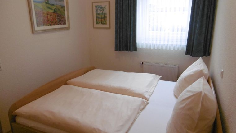 Ein gemütliches Schlafzimmer mit einem Doppelbett und zwei einzelner Kissen. Das Fenster lässt viel Tageslicht herein und ist mit hellen Vorhängen dekoriert.