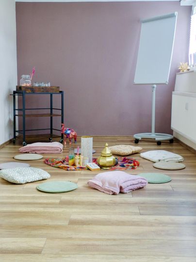 Une pièce accueillante avec des coussins colorés et des décorations sur le sol. À l'arrière-plan, il y a un paperboard et une table avec d'autres fournitures.