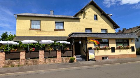 Ein gelbes Gebäude mit einem einladenden Restaurant und einer Terrasse. Parasols und eine deutsche Flagge sind sichtbar.