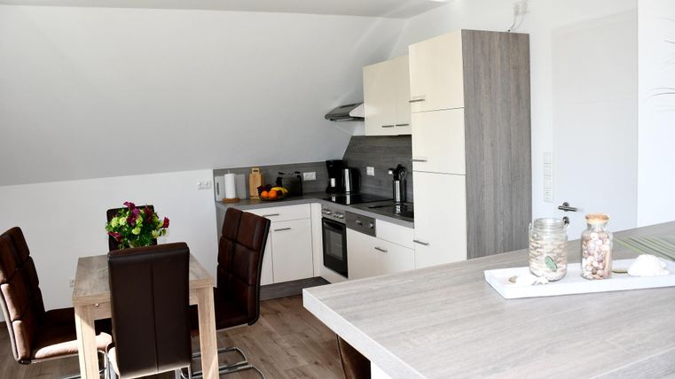 A modern kitchen with a dining table and cozy chairs. Bright colors and plenty of daylight create an inviting atmosphere.