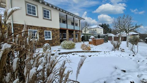Een mooi huis met een tuin die bedekt is met sneeuw. De lucht is helder en er zijn enkele wolken.