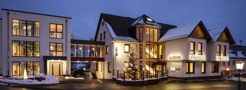 A modern hotel building with warm light and snow-covered ground. It is night and the architecture is inviting.