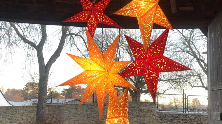 Bunte Sterne aus Papier hängen dekorativ in der Luft. Sie leuchten in warmen Farben und schaffen eine festliche Atmosphäre.