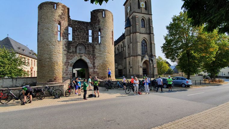 Groep fietsers voor een historische poort en een kerk.