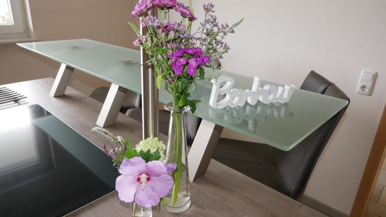 Een moderne eetruimte met een glazen tafel en stijlvolle stoelen. Verse bloemen in vazen en een decoratief bord vullen de gezellige sfeer aan.