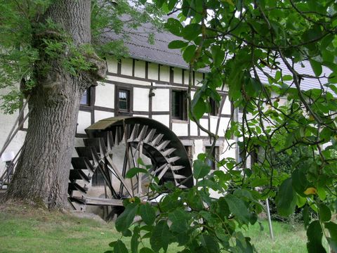Fachwerkhaus mit Mühlenrad und Baum im Vordergrund.