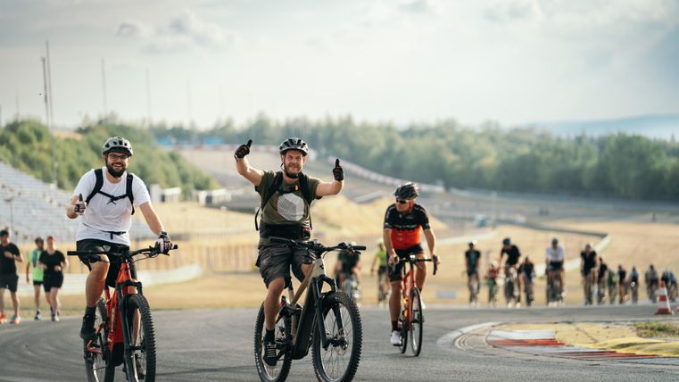 Eine Gruppe von Radfahrern fährt fröhlich auf einer Rennstrecke. Die Atmosphäre ist lebhaft und sportlich.