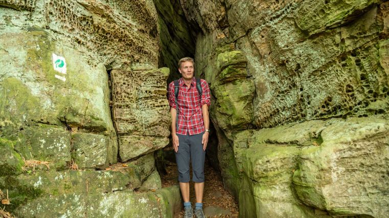 Person in plaid shirt standing in narrow rocky gorge.