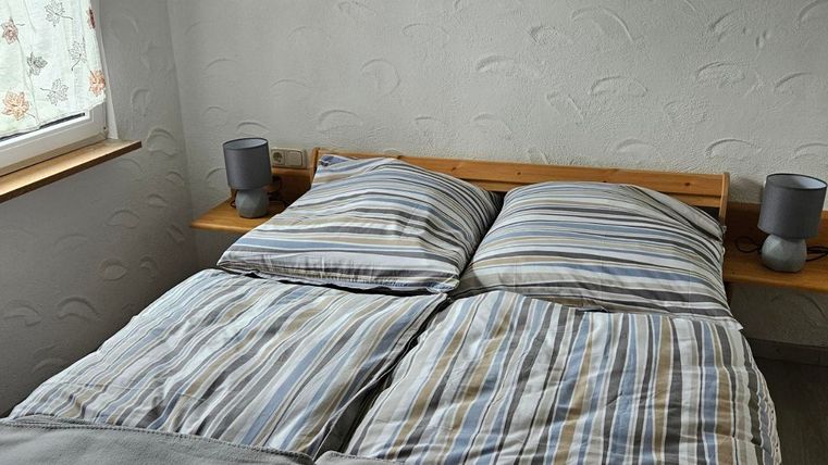 A cozy bedroom with a double bed and striped bedcovers. The walls are light, and a small picture hangs above the bed.