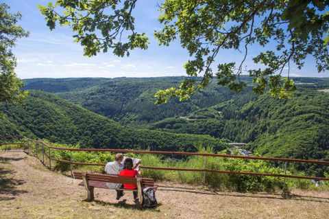 Een paar zit op een bank en geniet van het uitzicht op het groene dal. De lucht is blauw en het landschap is weelderig en heuvelachtig.