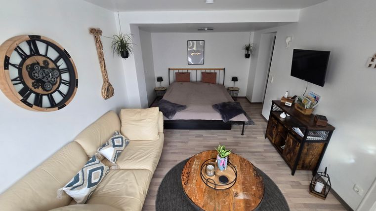 Een moderne kamer met een comfortabele bank en een groot bed. Aan de muur hangen decoratieve elementen, en een rond tapijt ligt op de vloer.