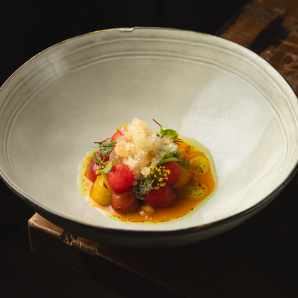 An elegant dish in a white bowl, richly garnished with colorful tomatoes and herbs. On top is a layer of ice that adds freshness to the dish.