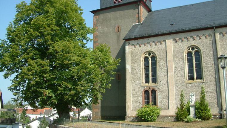 Parish church in Laufeld with tree and blue sky.