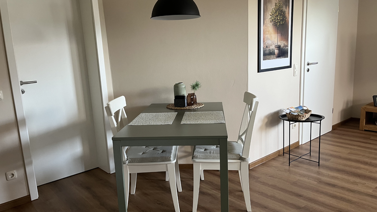 Une salle à manger confortable avec une petite table et deux chaises. Les murs sont clairs, et une image moderne est accrochée au-dessus de la table.
