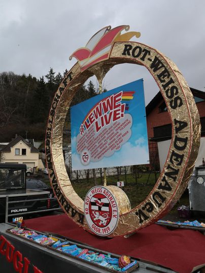 A festive setting with the inscription "Rot-Weiß Adenau" and a colorful display. In the background, houses and a cloudy sky can be seen.