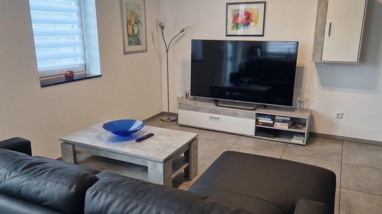 Un salon moderne avec un grand téléviseur et une table basse élégante. Les murs sont clairs et il y a quelques éléments décoratifs.