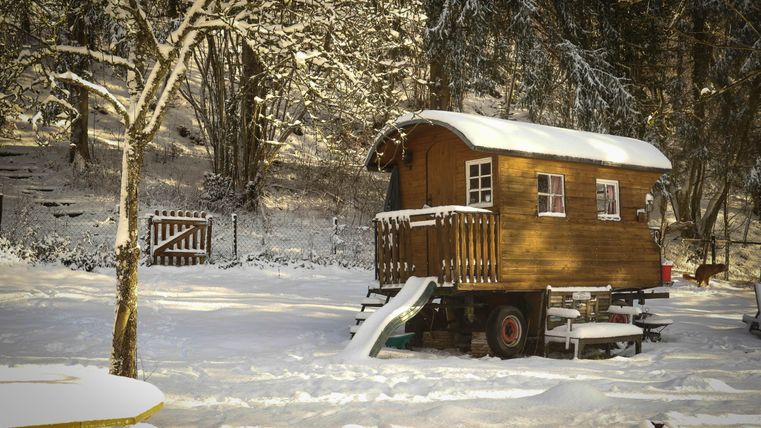 Ein gemütliches Holzhaus im Schnee, umgeben von Bäumen. Der Garten ist mit frischem Schnee bedeckt und es gibt einen kleinen Rutschbahn.