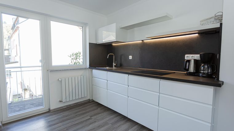 A modern kitchen with white cabinets and a dark work area. Large windows provide plenty of daylight.
