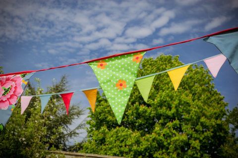 Bunte Wimpel wogen sanft im Wind vor einem strahlend blauen Himmel. Im Hintergrund sind grüne Bäume sichtbar.