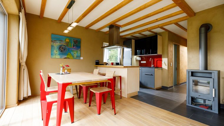 A modern dining room with a red table and chairs. The large window front provides plenty of daylight and a cozy atmosphere.