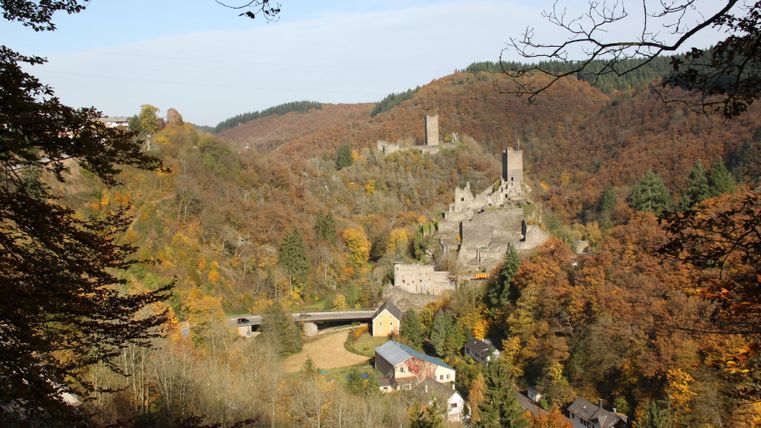 View of the Manderscheid castles in autumn with colorful foliage and surrounding hills.
