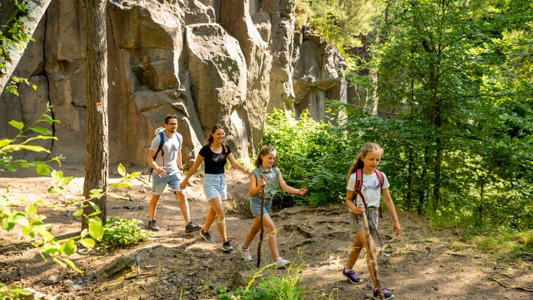 Familie wandert auf einem Waldpfad mit Felsen im Hintergrund.