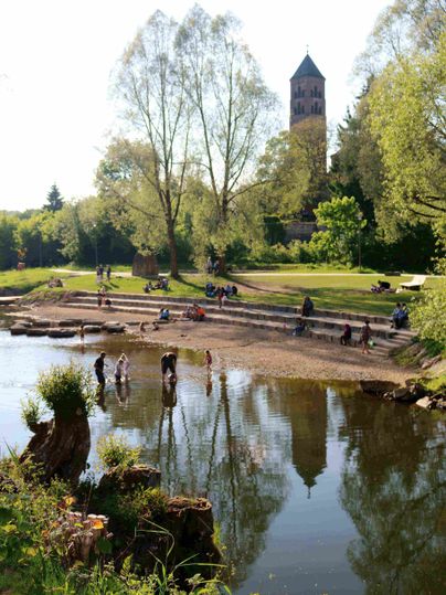 Mensen genieten van een zonnige dag in Kyllpark met een kerktoren op de achtergrond.