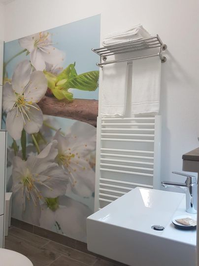 Ein modernes Badezimmer mit einer Wanddekoration von Blüten und einem stilvollen Waschbecken. Handtücher und ein Handtuchhalter sorgen für eine praktische und ansprechende Einrichtung.