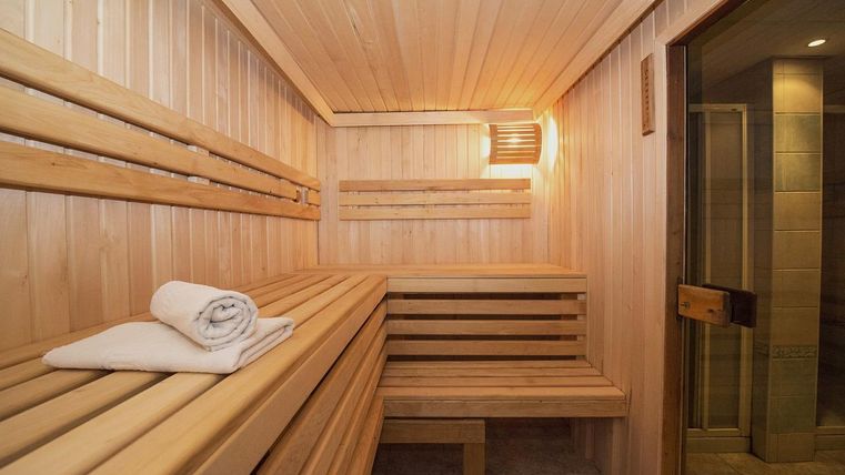 Eine helle Sauna mit Holzbänken und sanfter Beleuchtung. Ein frisches Handtuch liegt bereit.