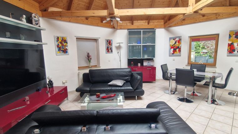 Un salon au design moderne avec des canapés noirs et une grande télévision. La pièce a des plafonds en bois et des œuvres d'art colorées aux murs.