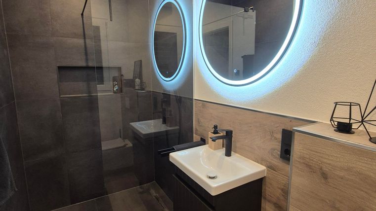 A modern bathroom with a walk-in shower and a stylish sink. The round mirror with indirect lighting adds an elegant atmosphere to the space.