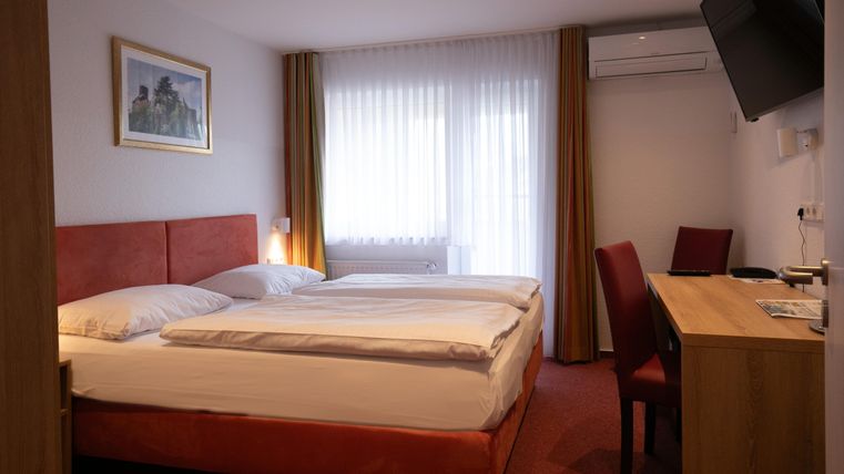 A cozy hotel room with a double bed and a desk. Large windows provide plenty of natural light.