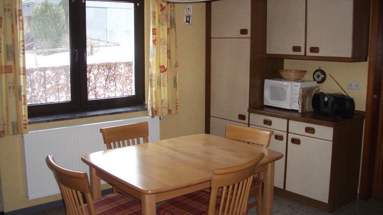Une cuisine confortable avec une table en bois et des chaises. À l'arrière-plan, il y a une fenêtre et quelques placards de cuisine.