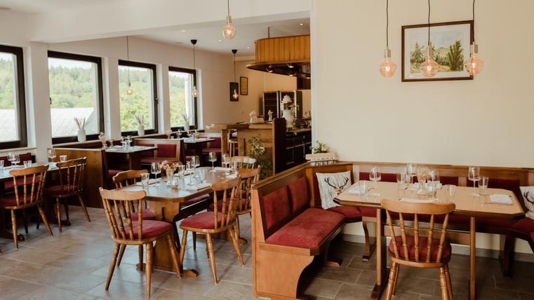 Ein modernes Restaurant mit Holzstühlen und Tischen. Die große Fensterfront sorgt für viel natürliches Licht.