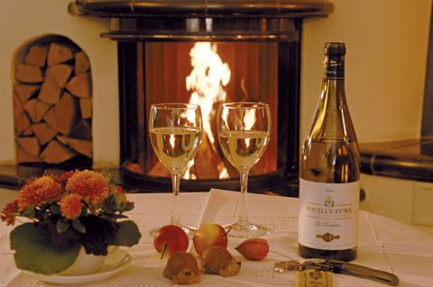 Een gezellige tafel met twee wijnglazen, een fles champagne en verse appels. Op de achtergrond brandt een open haard en zorgt voor een warme sfeer.