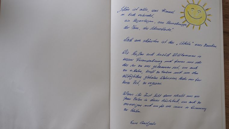 Ein offenes Buch mit handgeschriebenem Text und einem lächelnden Sonnensymbol. Die Seite auf der linken Seite ist leer, während die rechte Seite den Text enthält.