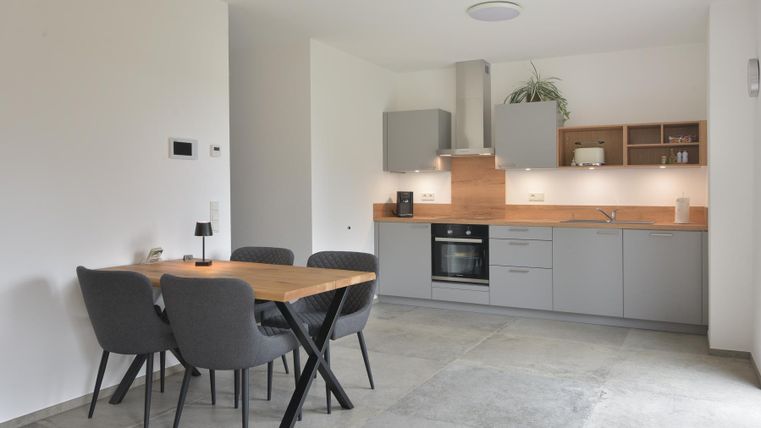 Eine moderne Küche mit grauen Schränken und einem Holzarbeitsplatz. Ein Esstisch mit Stühlen steht in der Mitte des Raumes.