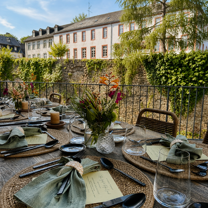 A beautifully set table outdoors with a view of a historic building. The table decoration includes green napkins, pretty flowers, and elegant glasses.