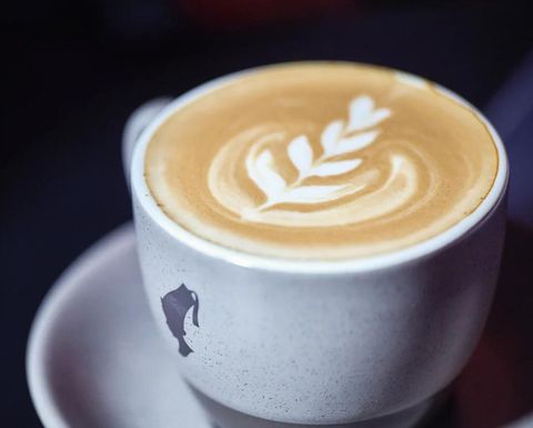 A cup of coffee with beautiful latte art in the shape of a leaf. The mug has a simple, modern design.