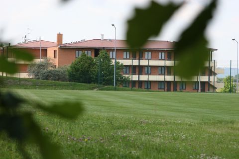 A modern building with several floors stands in a green landscape. Surrounded by meadows and trees, it appears inviting and tranquil.