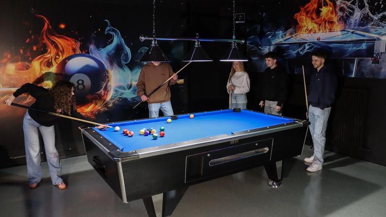 Een groep van vier personen speelt biljart aan een blauwe tafel. Op de achtergrond zijn kleurrijke, dynamische grafieken te zien.