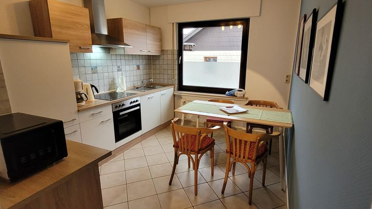 Eine moderne Küche mit Holz- und weißen Schränken. Ein Tisch mit Stühlen steht neben einem Fenster, das viel Licht hereinfällt.