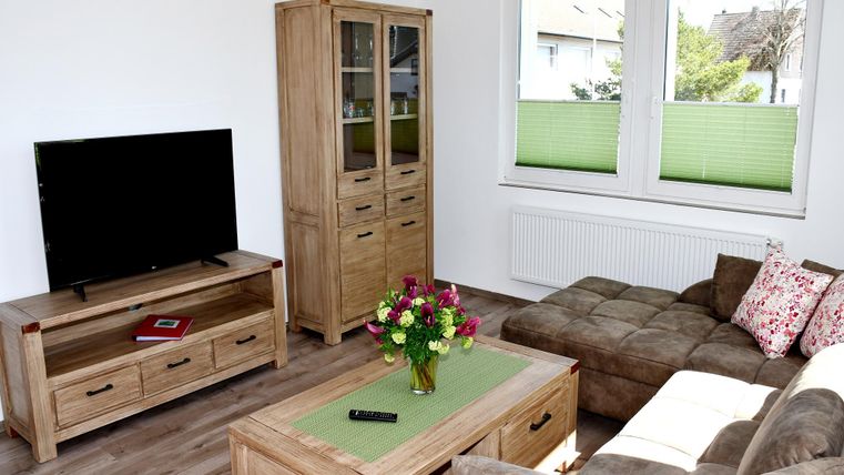 A modern living room with a television, an elegant wooden chest of drawers, and a comfortable sofa. On the table sits a vase with colorful flowers.
